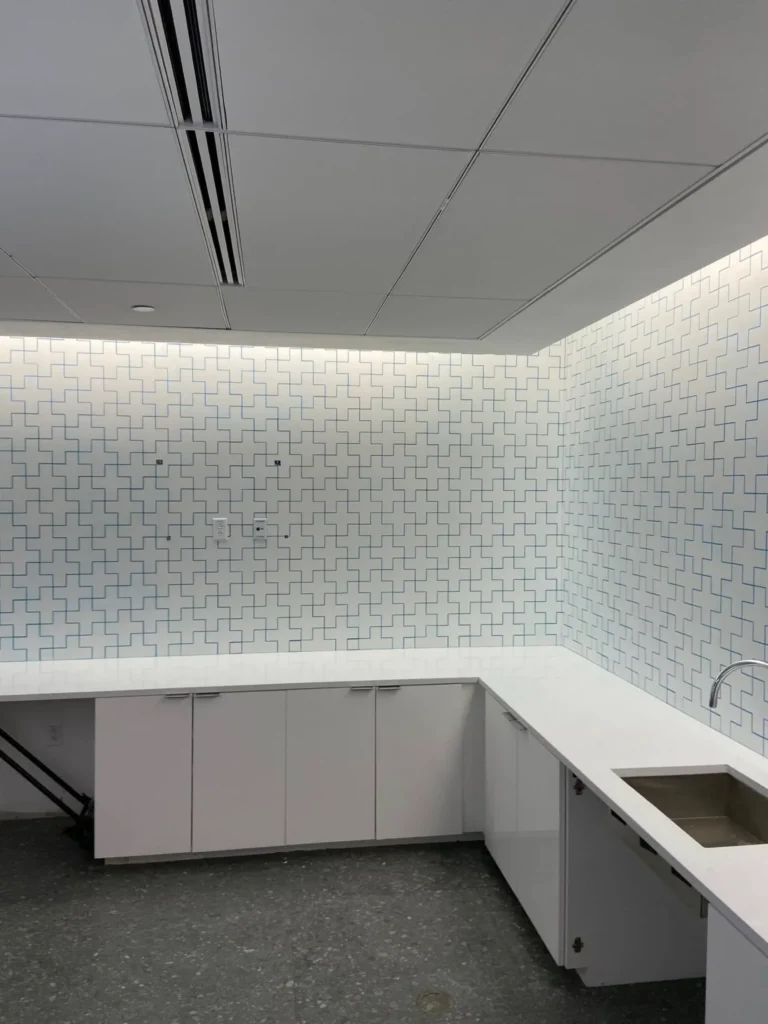 Commercial breakroom white interlocking cross pattern mosaic tile backsplash installation with blue grout lines and white cabinetry by DMtilellc in Hartford CT