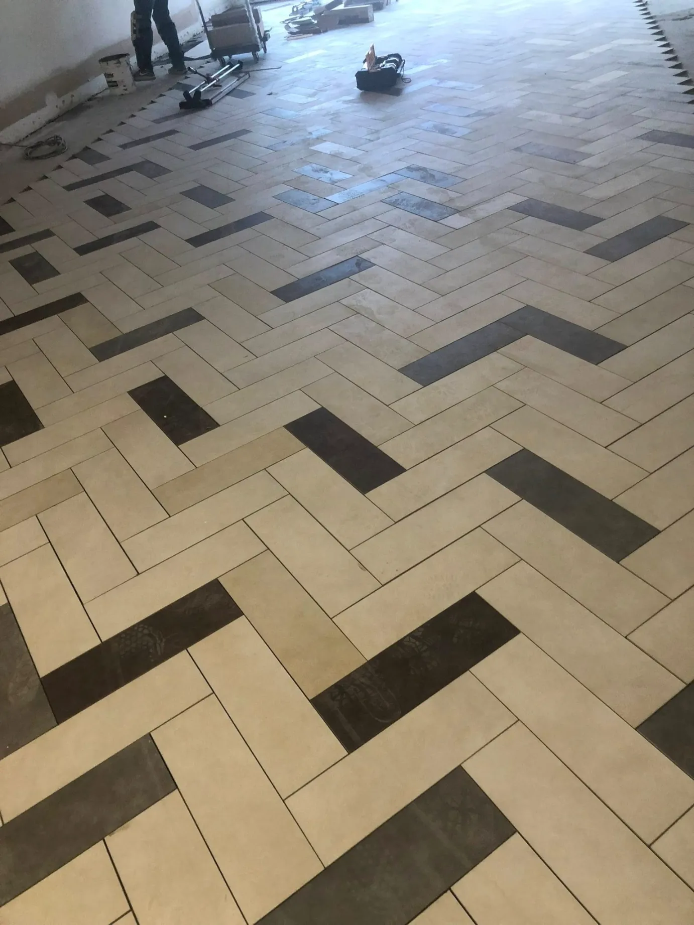 Large format herringbone pattern porcelain floor tile installation with dark accent planks on a commercial job site by DMtilellc in Greenwich CT