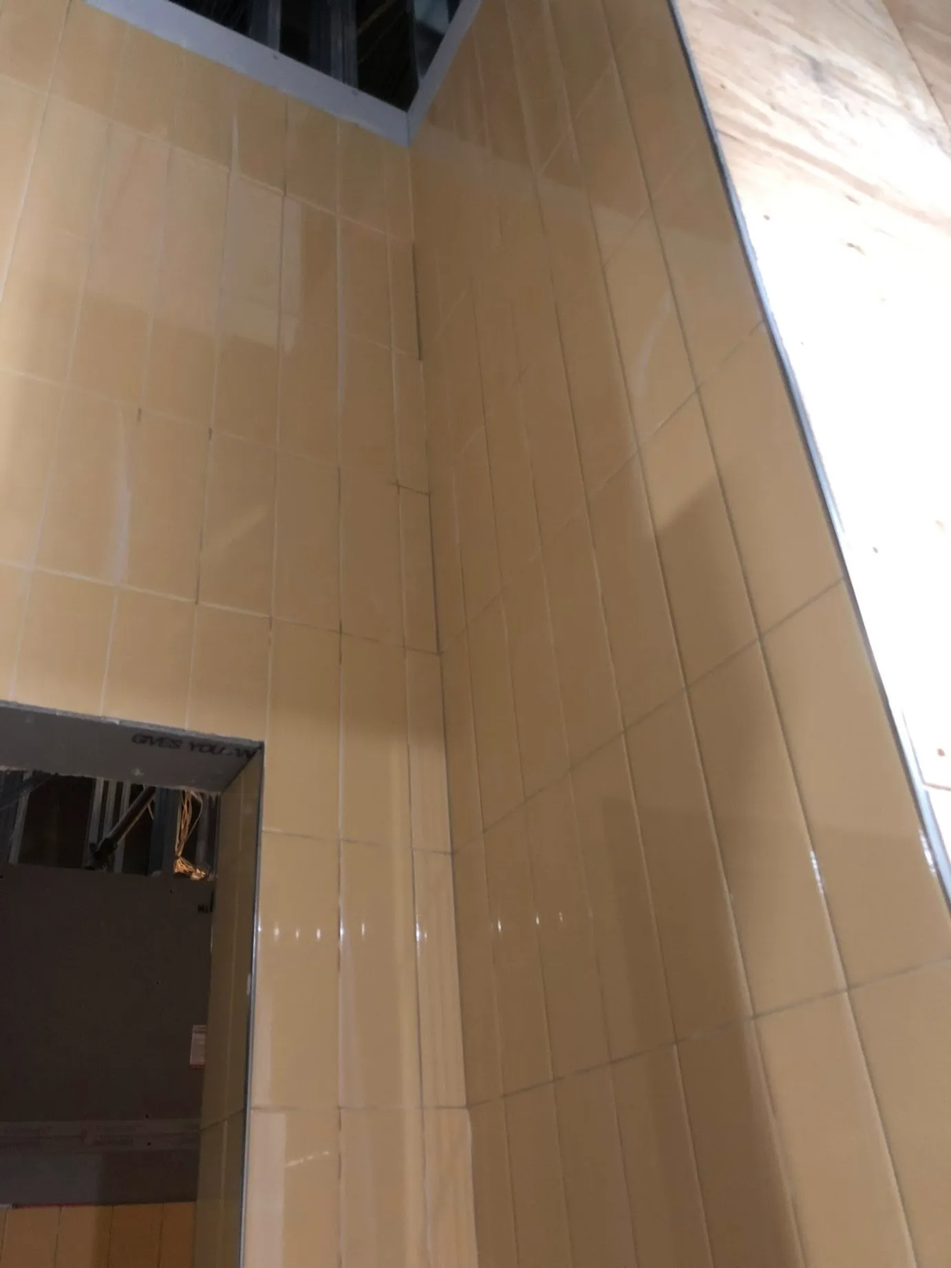 Vertical stacked beige ceramic wall tile installation around a doorway header on a commercial construction site by DMtilellc in Milford CT