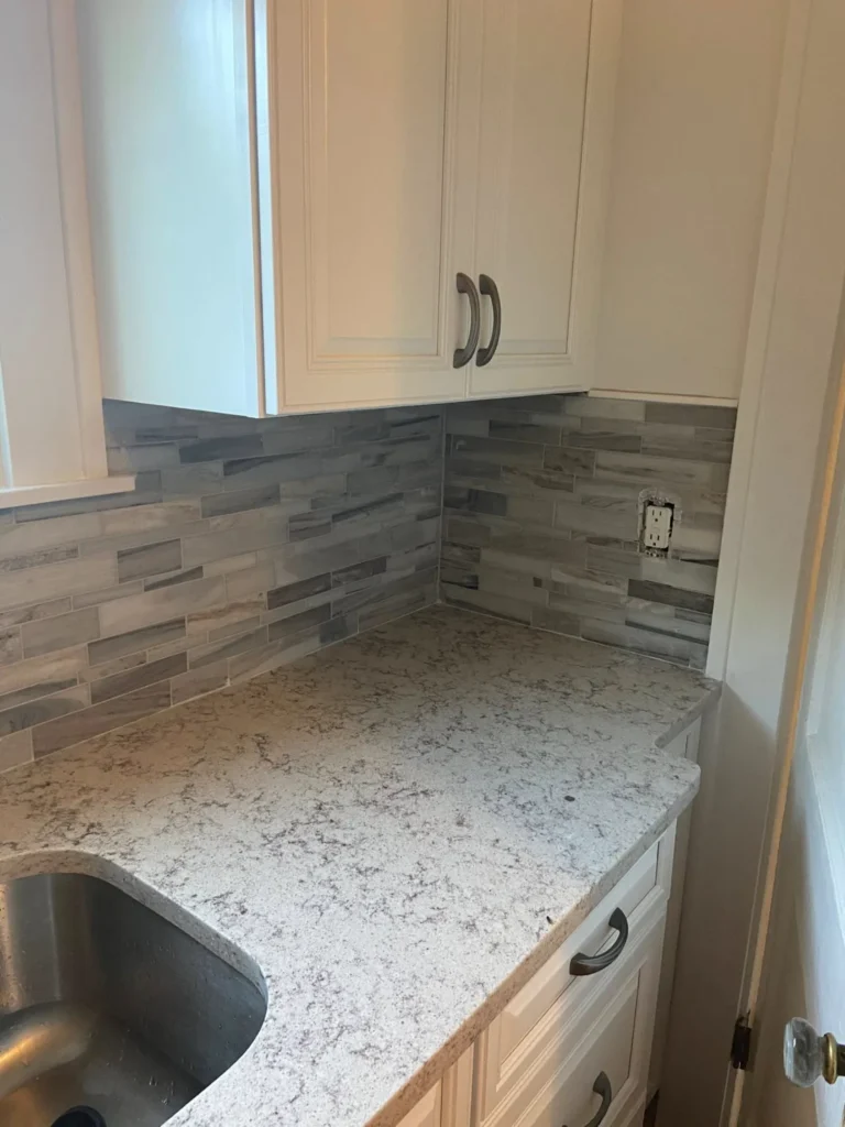 Gray linear stone mosaic tile kitchen backsplash installation featuring clean corner cuts and quartz countertop matching by DMtilellc in Fairfield CT
