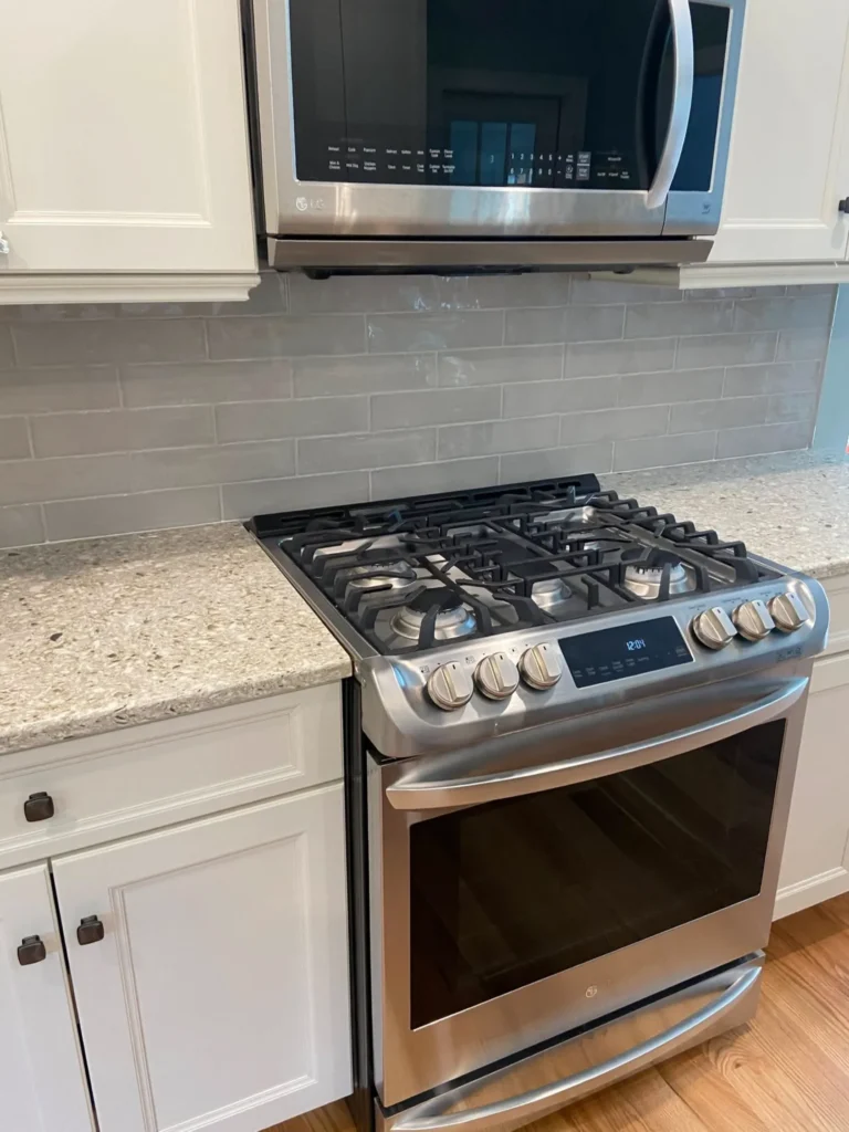 Gloss grey ceramic subway tile kitchen backsplash installation behind a stainless steel gas stove by DMtilellc in Stamford CT