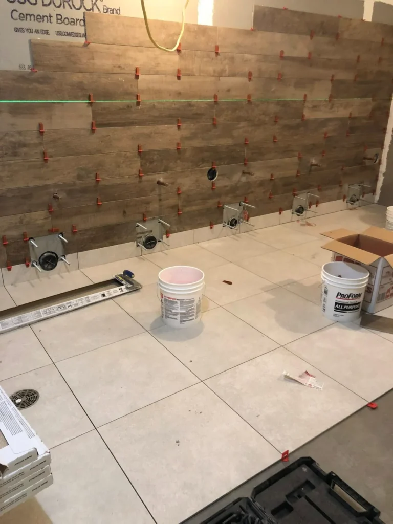 Wood-look porcelain plank shower wall tile installation using a laser level and orange wedge spacer clips over a large format tile floor by DMtilellc in Fairfield CT
