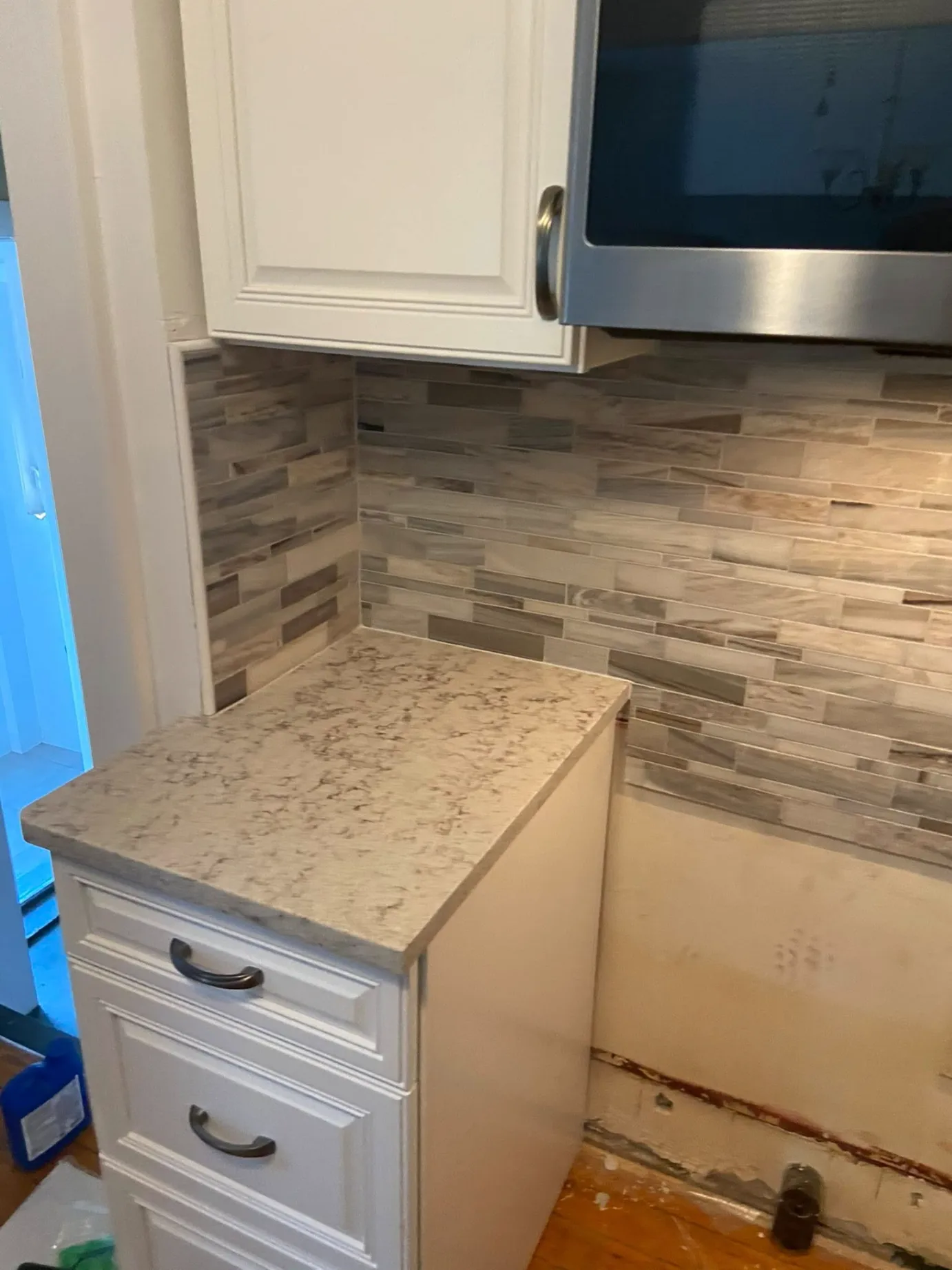 Linear stone mosaic tile kitchen backsplash installation with white cabinets and a neutral quartz countertop design by DMtilellc in West Hartford CT